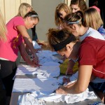 Members of the women's volleyball team – using forks, rubber bands and assorted techniques to effect unique designs – prepare shirts to be dipped in pink dye.
