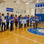 Cody E. Buterbaugh, representing the Student Athlete Advisory Committee, speaks during halftime of the men's basketball game and is joined at center court by the Fischer family, current and former members of the cross-country team, and members of the SAAC. Cody E. Buterbaugh, representing the Student Athlete Advisory Committee, speaks during halftime of the men's basketball game and is joined at center court by the Fischer family, current and former members of the cross-country team, and members of the SAAC.