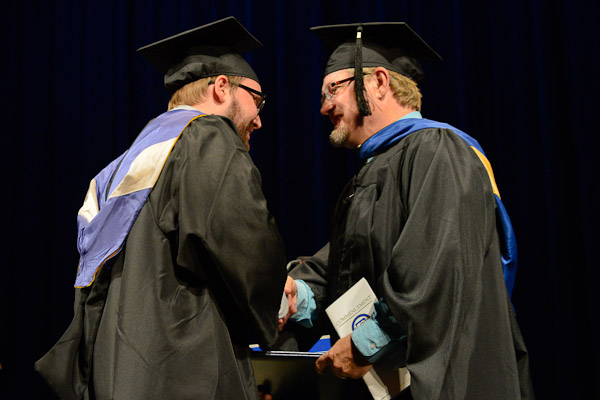 Graduating in business administration: human resource management concentration, Matthew D. Christopher shakes hands with proud father Daniel K., assistant professor of health information.