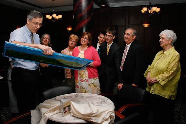 Thomas E. Ask, associate professor of industrial and human factors design, reads the inscription on the back of his hand-painted glass artwork that he presented to Michael S. Fischer's family. The painting, which depicts the rolling green hills that were the late cross-country runner's playground, is signed by Ask with the words: 