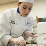 Baking and pastry arts student Kristina M. Williams adds chocolate “ribbons” to petit fours, a “gift” for guests following the meal.