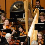 Colin W. Williamson (rear left) and Leah N. Nason (center foreground) join their symphony colleagues in performance on the CAC stage.
