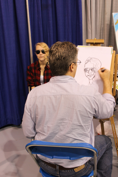 A caricaturist captures a cosplayer in Artist Alley.