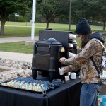 A student pours hot chocolate at Alumni Relations' homecoming hospitality table outside the Breuder Advanced Technology and Health Sciences Center.