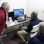 Mike Cunningham (seated) shows Marty Payne how to use the train simulation software on college-loaned computers.