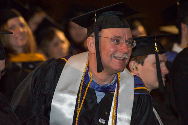 A new alumnus, clad in the varied colors of his academic achievement, offers a contented smile.