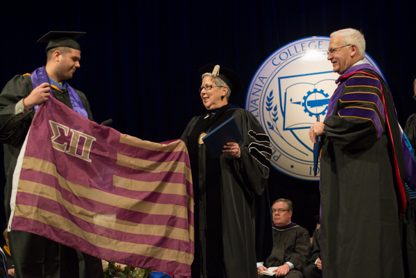 Jonathon L. Correll, who earned a bachelor's degree in legal assistant-paralegal studies, enlists the president in unfurling a Sigma Pi fraternity flag.