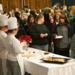 High school students gather around to watch baking and pastry arts students form roses from rolled chocolate.