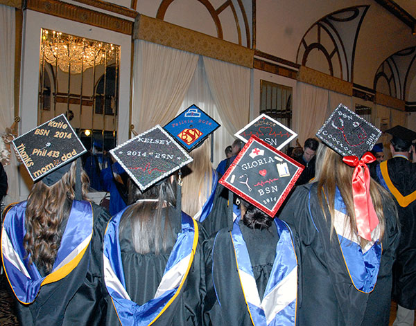 Four-year nursing graduates turn their eyes forward, allowing a look at their colorfully appointed mortarboards.