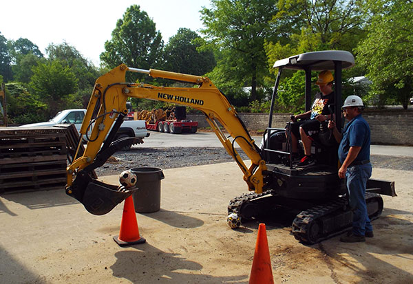 Ken J. Bashista, laboratory technician for diesel equipment technology, coaches a Career Day guest as he uses an excavator to lift a soccer ball from a cone and into a trash can.
