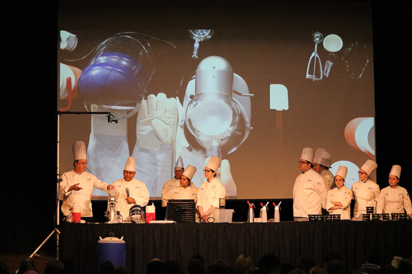 The big screen shows the equipment that will be used by audience volunteers when they “cook” with liquid nitrogen.