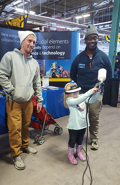 Admissions counselor Lee A. Dawson (right) watches a young guest wield a virtual-reality automotive paint-sprayer.