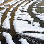 Tire tracks on a parking lot form an interesting criss-cross pattern as the morning snowfall makes a solar-powered surrender.