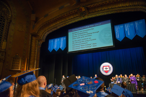 The words to the alma mater are projected on the big screen, giving grads the opportunity to musically recall their