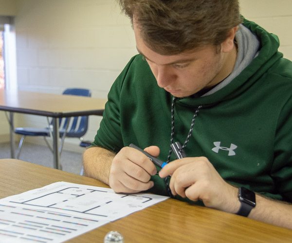 A student contemplates how he will instruct an Ozobot.