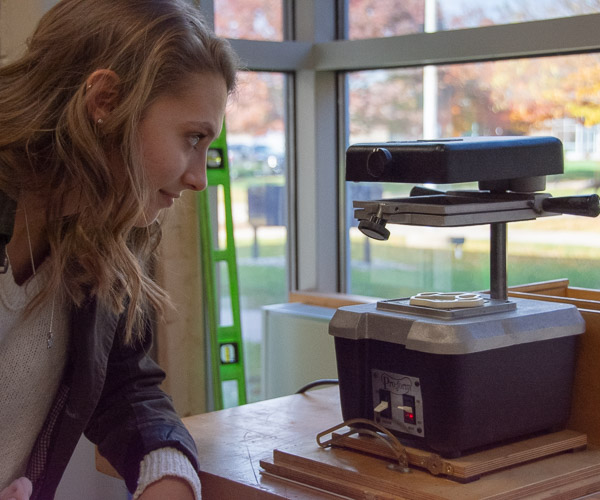 On a small-scale thermoformer, a high school student watches a thin sheet of plastic change properties as it reaches the ideal temperature to form it around a cat’s paw mold …