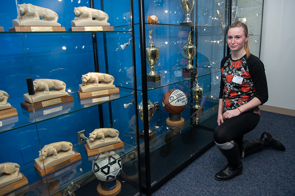 Obliging a photographer’s request, 2017 nursing grad Alicia N. Ross poses with the basketball touting her as the “Women’s All-Time Scoring Leader” with 1,515 points from 2014-17. The ball and other treasured trophies are displayed in the Athletics conference room.