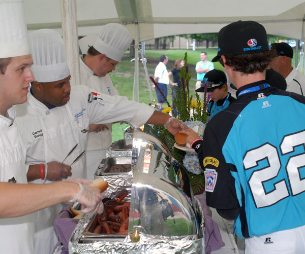 Players move through the food tent, amassing plates full of hot dogs, hamburgers and other picnic fare.