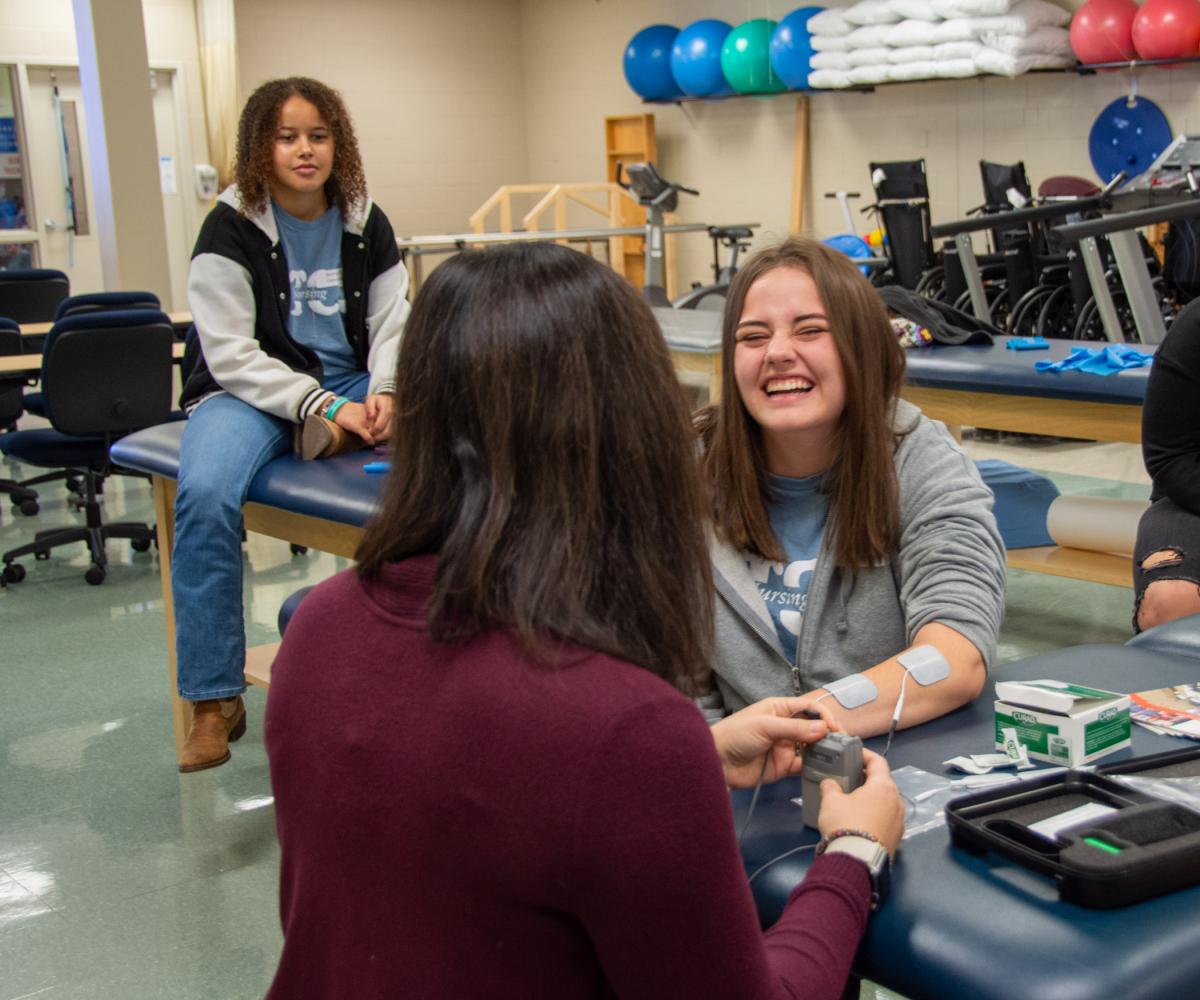 A visitor laughs at the sensation as Victoria Hurwitz, director of physical therapist assistant, administers the program’s neuromuscular reeducation unit, used to help patients regain use of their muscles.