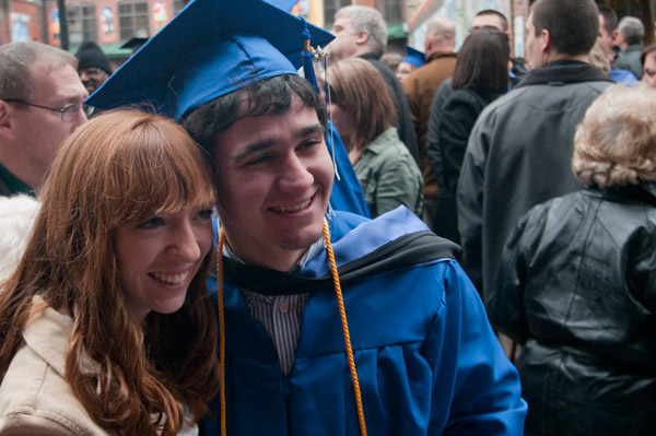 A graduate soaks in the moment with a loved one while posing for a camera.