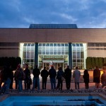 In the dusky blue of twilight, card-lighting attendees stand silhouetted outside the ATHS.