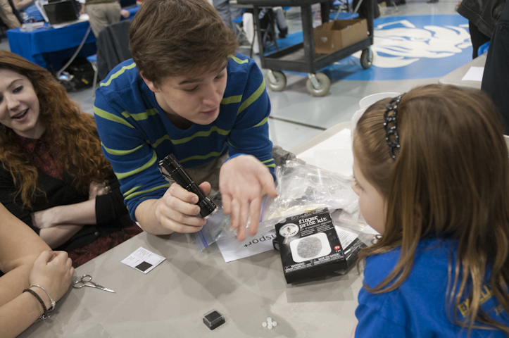 A high-schooler shows a younger student the science of UV light as it changes the color of several beads.