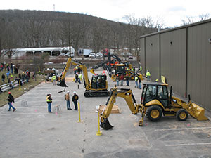 Competitors and judges move among heavy construction equipment assembled for a “rodeo” while parents and other spectators watch from bleachers outside the Schneebeli Earth Science Center during Penn College’s March 23 Open House.