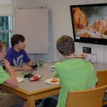 Campers unwind with refreshments and a game of Halo 2 in a library study room.