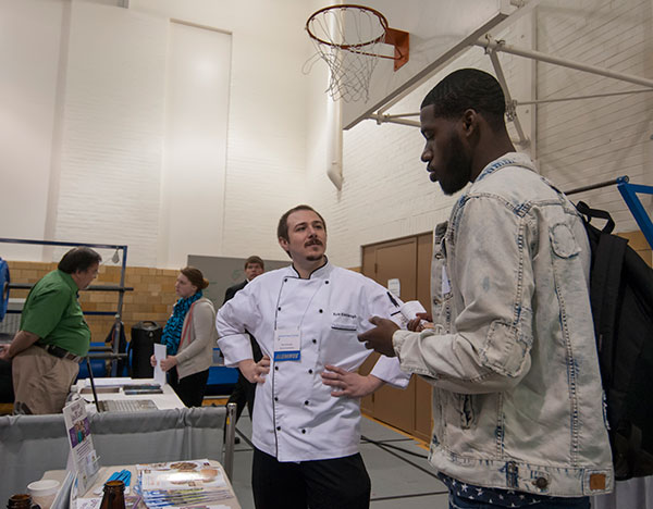 Kyle Kishbaugh, a 2009 culinary arts and systems grad, greets students at the Wegmans Food Markets display.