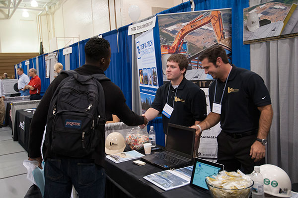 Wearing the blue ribbon that denoted alumni at the Career Fair,  2013 construction management graduate Michael R. Caulfield shakes hands with a visitor to the Lobar Associates Inc. booth.