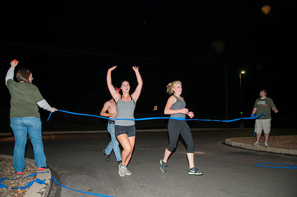 Runners cross the finish line, held by Allison A. Bressler, assistant director for student activities for programming and Greek life, and student Derek E. Teay.