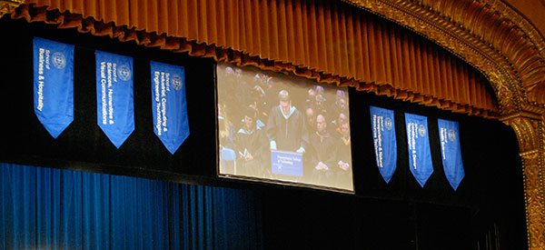 Flanked by banners from Penn College's six academic schools, a projection screen helps attendees watch the proceedings.