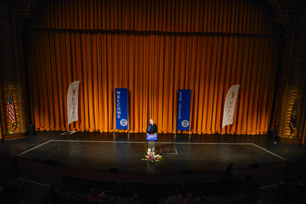 Flanked by college and centennial banners, President Gilmour welcomes the campus community to the evening's presentation.