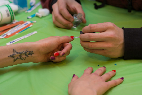 A fraternity member applies a sheer topcoat to alternating red and purple nails.