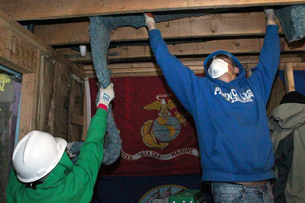 Volunteers install insulation, with a Marine Corps banner to remind students of the building's future occupants.