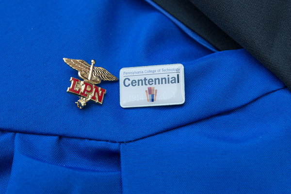 A Centennial keepsake mingles with a Licensed Practical Nursing pin on a graduate's gown.