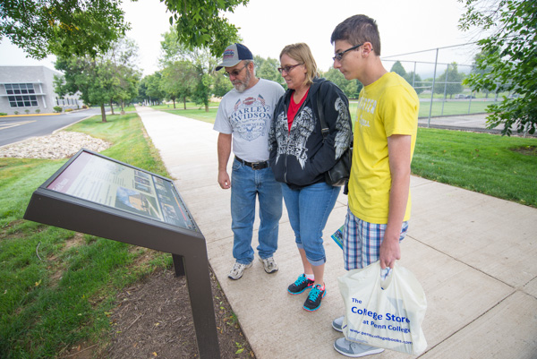 After moving in and shopping at The College Store, Allen M. Atland, a freshman enrolled in information technology: technical support technology emphasis from York, pauses with his family to take in a History Trail marker near the Field House. 