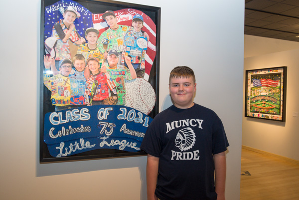 Logan Rakestraw stands next to the piece he created last year with fellow fifth-graders at Ward L. Myers Elementary School in Muncy. Rakestraw's image can be seen in the artwork in the far right (green shirt next to the baseball) of the first row.