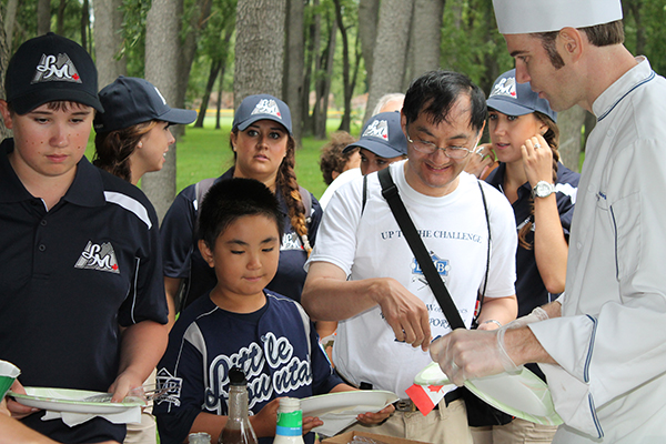 Players and supporters of the Little Mount Little League team from Vancouver, British Columbia – participants in the Challenger Division exhibition game – gather their plates for a picnic lunch coordinated by business administration professor Steven J. Moff and served by students in the School of Business & Hospitality.