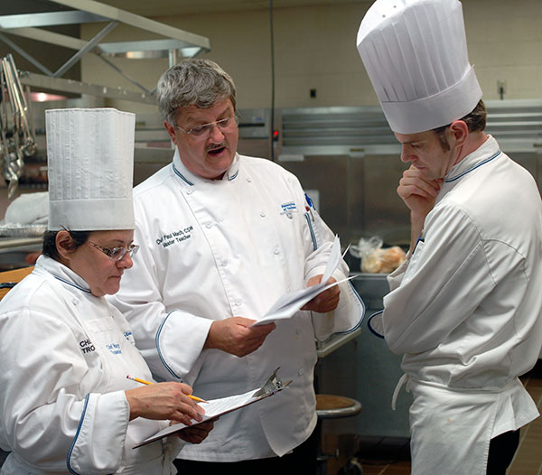 Reviewing their judging criteria during the students' preparatory time are (from left) Chefs Mary G. Trometter, assistant professor of hospitality management/culinary arts; Mach; and Charles R. Niedermyer, instructor of baking and pastry arts/culinary arts.