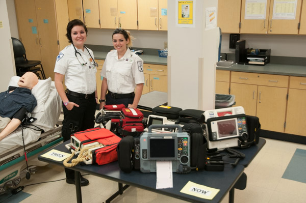 Emergency Medical Services students Crystal E. Van Aken, of Emmaus, and Kierstin M. Slesienski, of Bensalem, stand ready to greet the community with a display of defibrillators from the 1980s through today.