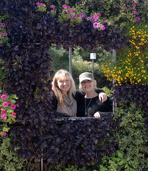 Cousins Rebecca A. Clawson (left), a 2004 biology alumna, and Angela Sweely, a 2008 graduate in architectural technology, pose amid the seasonal color of the college's vertical gardens. Clawson is planning the Pennsylvania Association for Sustainable Agriculture's 