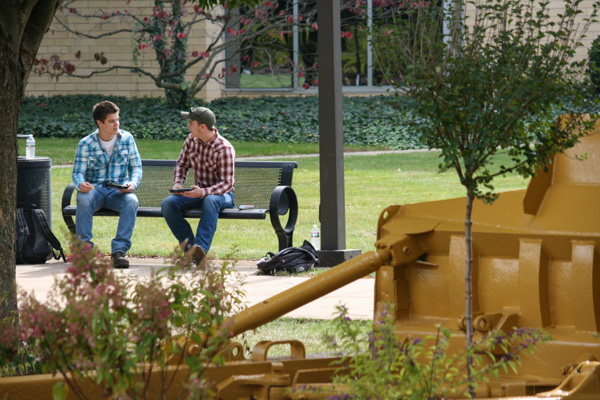 Freshmen Luke T. Lesuer (left) and Travis M. Brownlee, on a bench near a commemorative construction blade to enjoy conversation and picnic fare following the “Student Bodies” dedication. Lesuer, from Cambridge Springs, is enrolled in welding and fabrication engineering technology; Brownlee, from Claysville, is a welding technology student.  