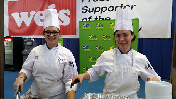Culinary arts and systems majors Brianna E. Bucklin (left), of Whitehall, and Victoria L. Zablocky, of Jersey Shore, serve vegetable-filled hush puppies and slaw to audience members.