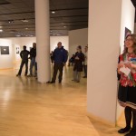 The crowd – including gallery manager Penny G. Lutz (right), colorfully dressed to complement the exhibition – listens to the artist's remarks.