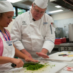 Chef Frank M. Suchwala, assistant professor of hospitality management/culinary arts, helps a student learn knife skills as she minces parsley.