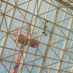 Tethered to a lift and shod in suction cups, a worker diligently refurbishes the skylight's skeleton.