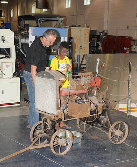 Ten-year-old Monroe takes his turn starting a vintage automobile engine, helped by collision repair instructor Roy H. Klinger.