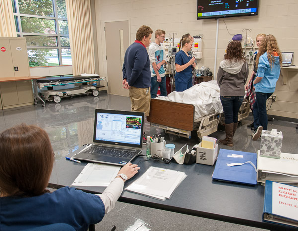 A group of high school students watch the lifelike reactions of SimMan, operated from a laptop.