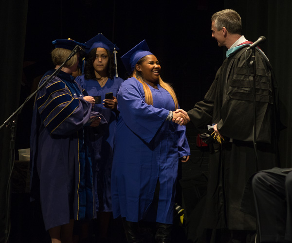 Michael J. Reed (right), interim dean of sciences, humanities and visual communications, shakes hands with his school’s graduates. 